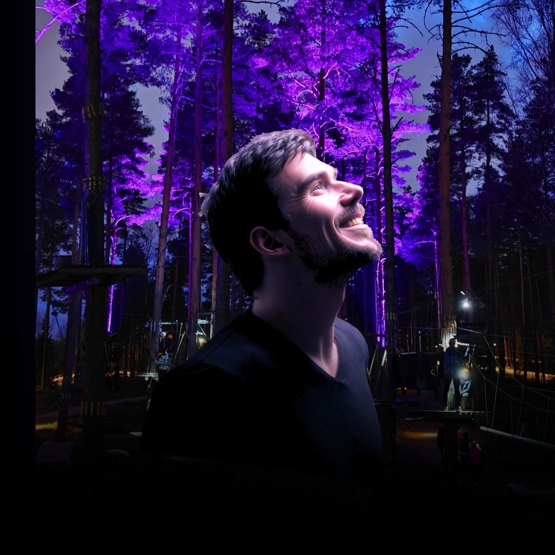 Giant life-size head of a smiling man, installation in a purple-lit forest at night.